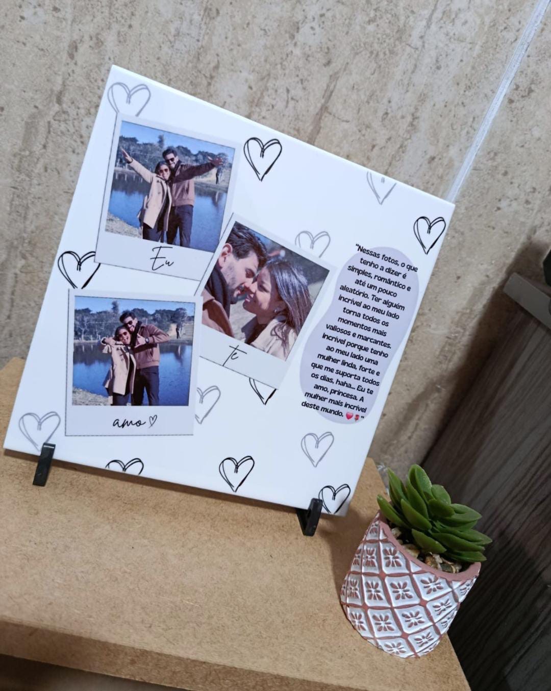 Azulejo branco em suporte, com três fotos de casal em estilo polaroid com as palavras Eu te amo, corações e uma mensagem de amor